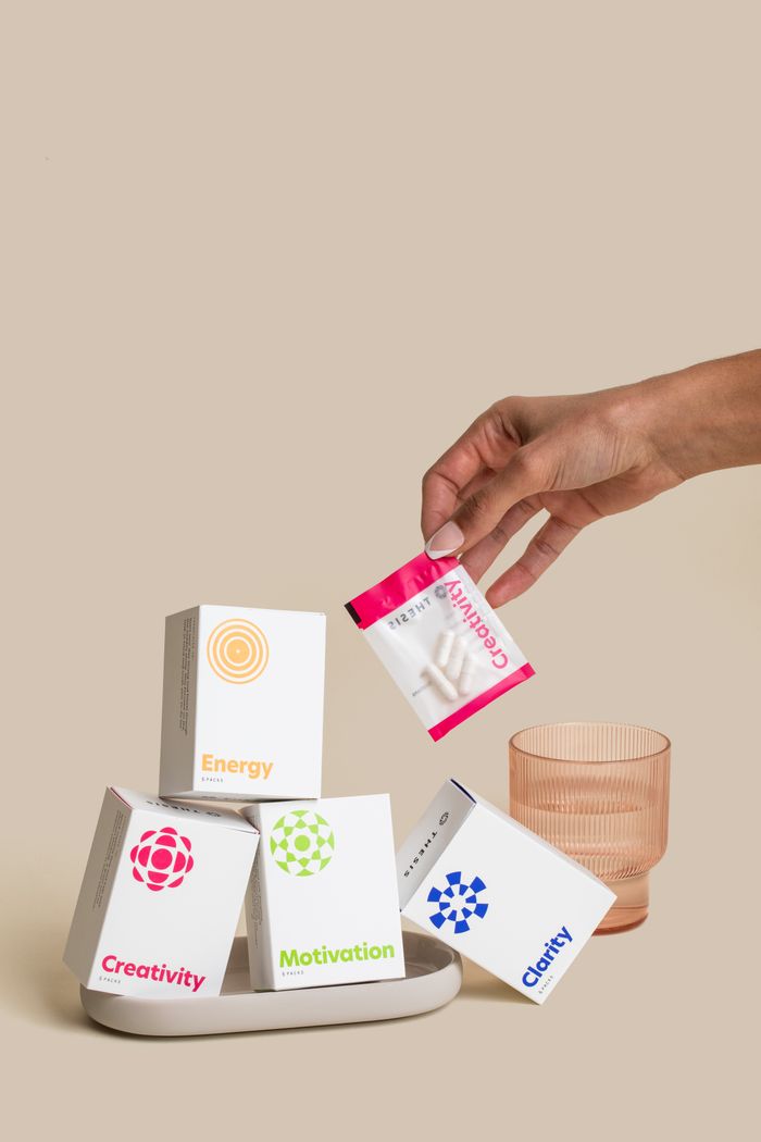 Hand holding a sachet above a stack of supplement boxes with glass, symbolizing vitamins.