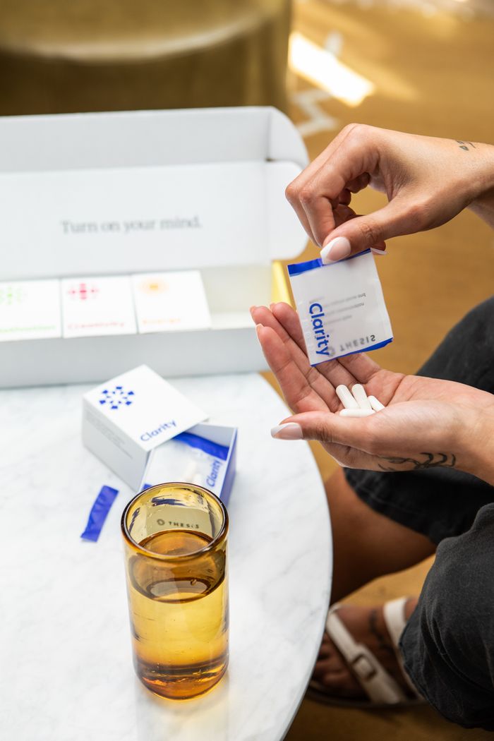 Close-up of hands holding supplement sachets with a box and glass on table.